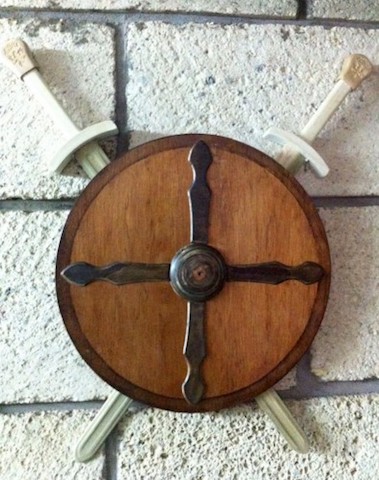Escudo de madera con diseño de cruz y espadas montadas en la pared.