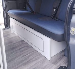 Asiento de furgoneta camper con tapicería azul y compartimento de almacenamiento blanco, sobre suelo laminado gris.