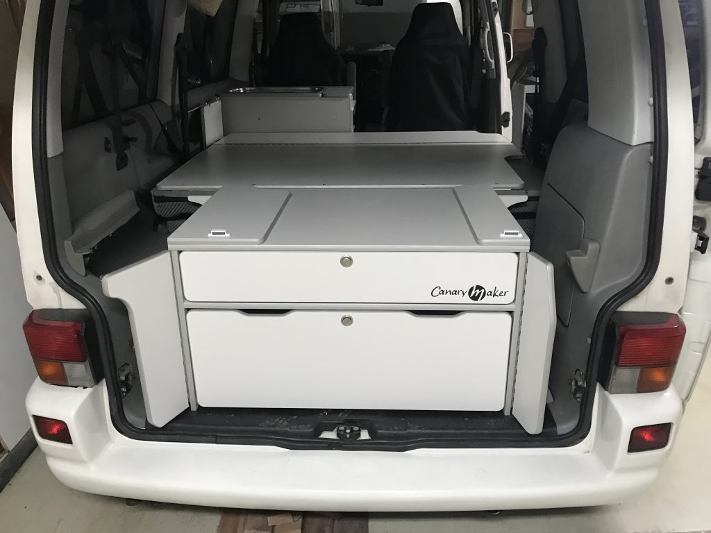 Vista trasera del interior de una furgoneta camper con mueble de almacenamiento blanco y espacio de encimera.