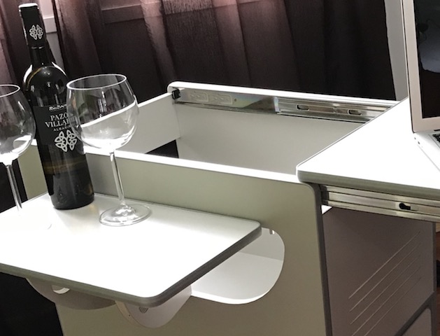 Interior de una furgoneta camper con una mesa plegable, una botella de vino y dos copas, junto a una nevera integrada.