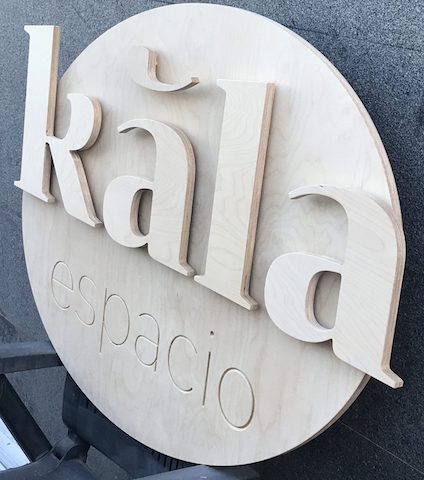 Rótulo de madera con las palabras 'Kala espacio' en relieve, montado sobre una pared exterior.