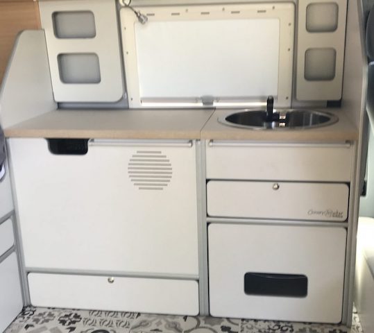 Mueble de cocina blanco en una furgoneta camper con fregadero y almacenamiento integrado.