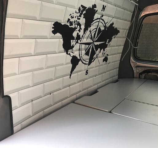 Interior de una furgoneta camper con papel de pared de ladrillo blanco y una decoración de mapa mundial con brújula.
