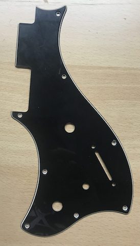 Golpeador negro para guitarra con varios orificios y cortes, sobre una superficie de madera clara.