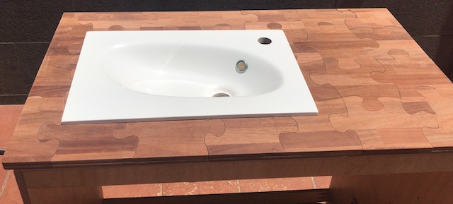 Encimera de baño con diseño de puzzle en madera, integrando un lavabo blanco.
