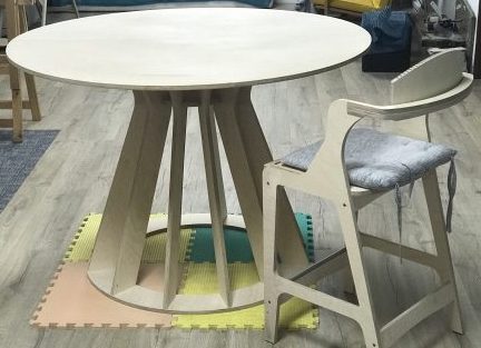Mesa alta redonda con base central de madera y taburete a juego en un espacio de trabajo.