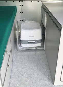 Inodoro portátil Thetford ubicado en un compartimento específico de un mueble camper dentro de una furgoneta.