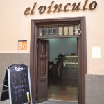 Entrada de madera a 'El Vínculo', un establecimiento, con un cartel de tiza anunciando tapas y vinos.